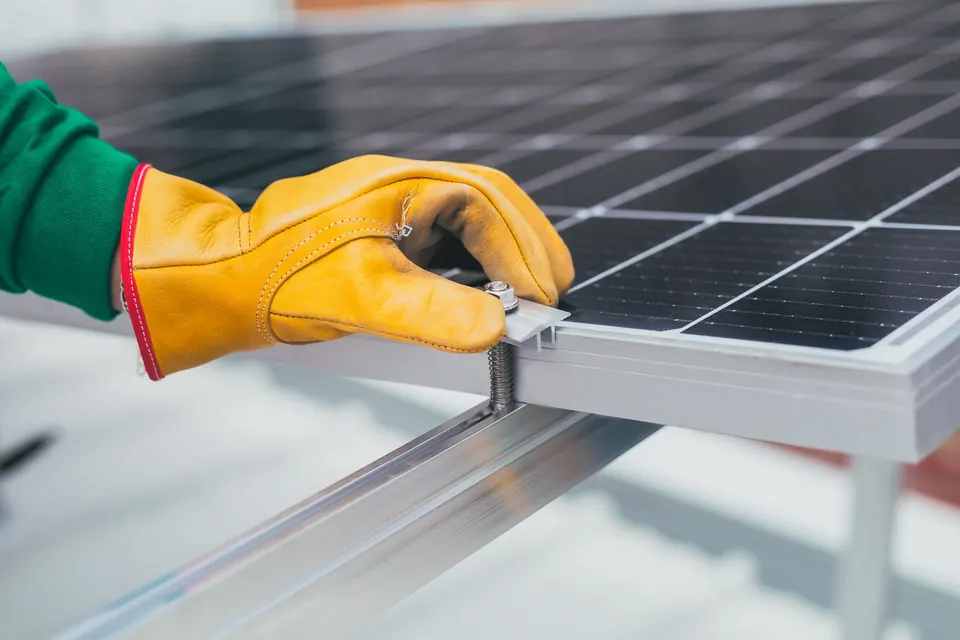 Main gantée serrant la bride qui fixe un module photovoltaïque sur son rail