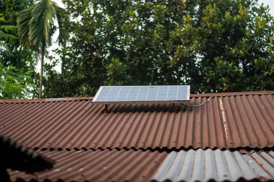 Petit panneau solaire sur une toiture en tôle ondulée, arbres tropicaux derrière