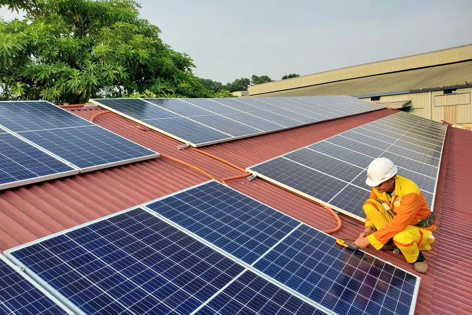 Technicien casqué raccordant des panneaux photovoltaïques sur une toiture en tôle rouge